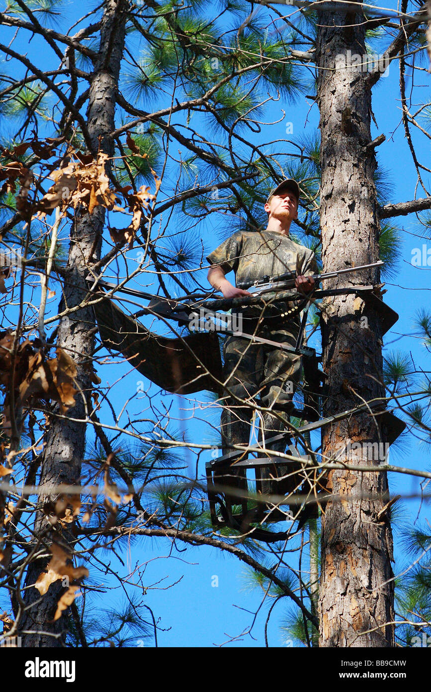 close-up-hunter-standing-in-tree-stand-holding-weapon-at-the-ready-BB9CMW.jpg